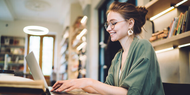 Cheerful Young Freelance Woman Typing on Laptop