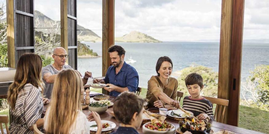 Want to Bring Your Family to New Zealand? We Can Help! Family Having Dinner in House by the Coast