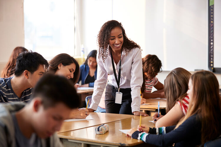 Female High School Teacher Standing by Student Table